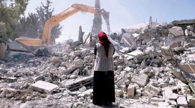 سيدة تقف أمام منزلها بعد أن تم قدمها من قِبل قوات الاحتلال
